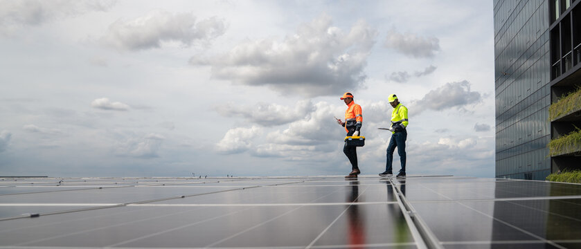 Solar Technicians Survey a Large Rooftop Photovoltaic Array While Reviewing Renewable Energy System Performance at a Commercial Building for Maintenance Planning
