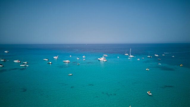 Numerous boats and yachts are dotting the clear turquoise waters, creating a vibrant scene of summer vacation and marine leisure activities along the coast of san vito lo capo, sicily, italy
