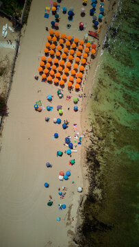 San vito lo capo beach in sicily, italy, showing an aerial view of many colorful beach umbrellas, people relaxing on the sand, and swimming in the clear blue green sea during summer vacation
