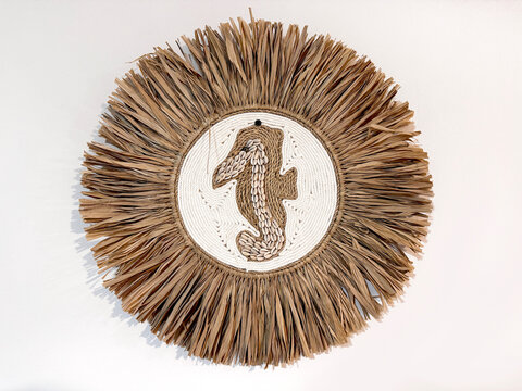 Close up a bohemian circular wall decor featuring a cowrie shell seahorse surrounded by a natural raffia fringe. Isolated on white background