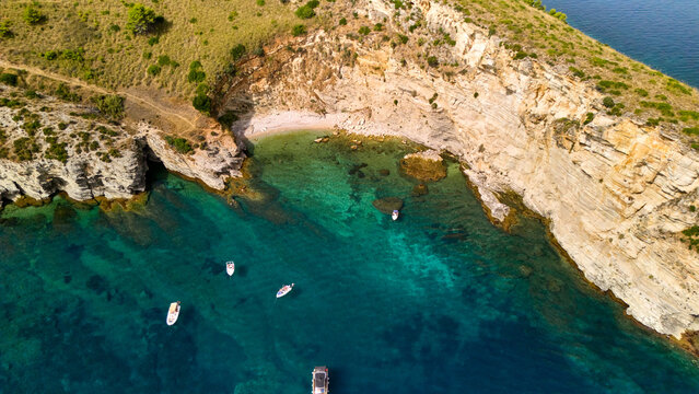 Turquoise water contrasting with rugged cliffs and a hidden beach, with small boats anchoring in the serene contrada conza bay, sicily