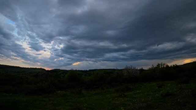 Time-lapse shot showing dark storm clouds forming and the onset of a summer rain shower over green hills and countryside.