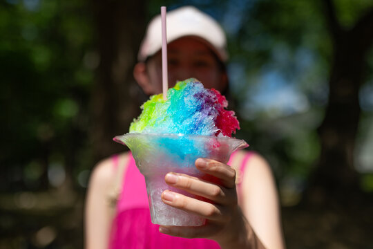 公園でカラフルなレインボーかき氷を差し出す顔隠しの女の子