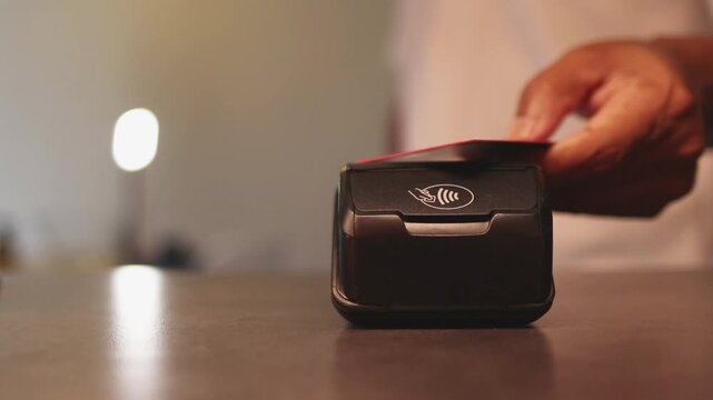Customer using contactless credit card for nfc electronic payment on pos terminal at checkout counter in a store or restaurant