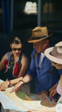 Three tourists are intently studying a map to plan their route in an urban setting. They are planning their city exploration, pointing out places of interest on the folded paper.
