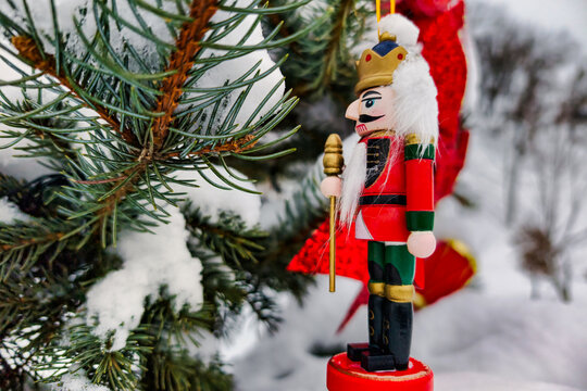 A Christmas tree stands in the snow. It is decorated with colorful ornaments and a nutcracker figure. The scene is festive for New Year and Christmas