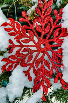 A Christmas tree stands in the snow with red decorations hanging from its branches as winter unfolds in the background