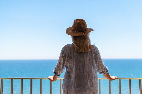 Woman in sun hat standing on balcony with panoramic Mediterranean Sea 