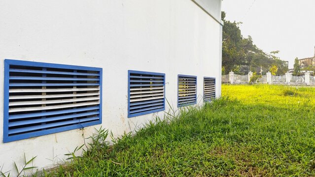 White building exterior wall with blue louver ventilation grilles and green grass