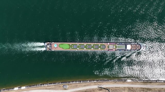 Aerial view of a river cruise ship with a sun deck, lounge chairs, and a small pool navigating the calm waters of the canal in Kembs, Grand Est, France.