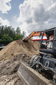 Heavy machinery works on a construction site. An excavator digs a deep trench with dirt being moved away in an urban environment