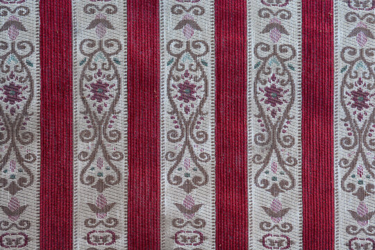 A top down close up shot of a retro textile pattern with red vertical stripes and ornate floral embroidery on beige bands.