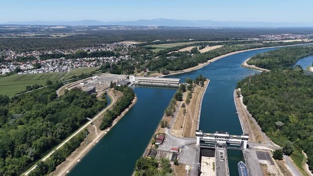 Aerial view of Kembs hydroelectric power plant and lock system on the Rhine river surrounded by lush forests and fields in Kembs, Grand Est, France.