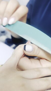Manicurist filing woman nails with nail file close up 9:16 vertical, beauty salon manicure treatment concept