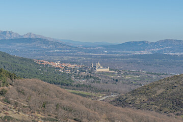Fototapeta premium Panoramic view of El Escorial monastery and town nestled in a valley surrounded by forested hills and distant mountains.