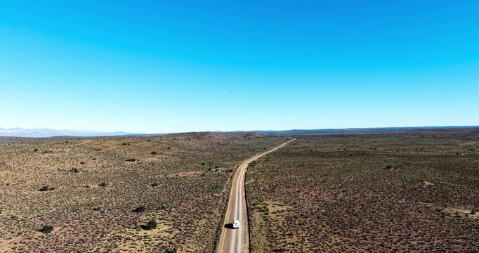 Drone view of a 4x4 vehicle travelling along a winding gravel road through the Great Karoo in South Africa. An expansive blue winter sky stretches toward the horizon capturing freedom and solitude.