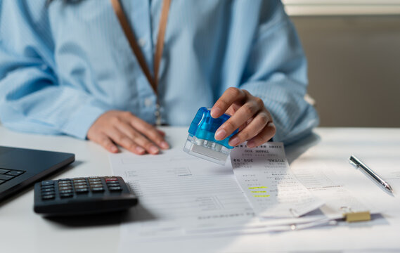 Business woman accountant hand stamping invoice receipt on office desk. Corporate professional doing financial paperwork verification with calculator and laptop for accounting audit.