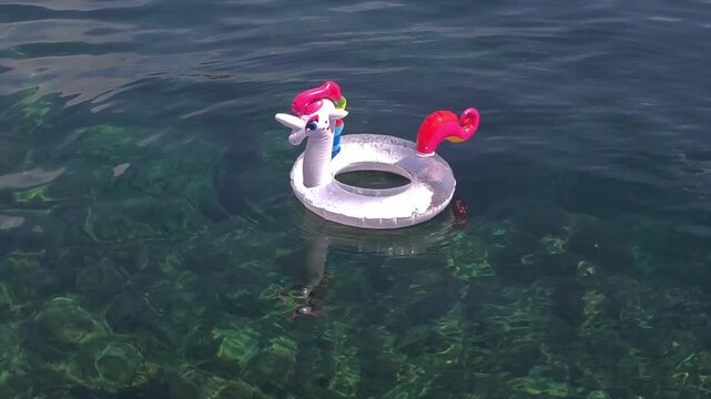 Transparent unicorn inflatable ring floating alone on crystal clear sea