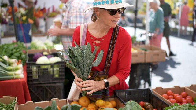 Happy senior woman purchases kale at the Sonoma Farmers Market on a bright day. The market is lively and colorful.