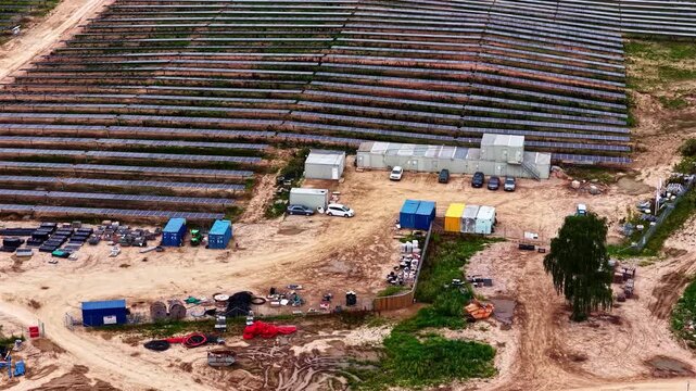 Aerial view of solar farm construction site with rows of solar panels, containers, and construction equipment on the ground in Tume, Tukums Municipality, Latvia.