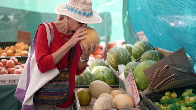 A woman enjoys selecting a cantaloupe and fresh produce at the Farmers Market in Sonoma, California on a sunny morning.