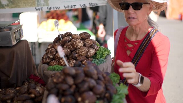 A senior woman smiles as she buys fresh shiitake mushrooms at a farmers market in Sonoma California on a warm sunny day.