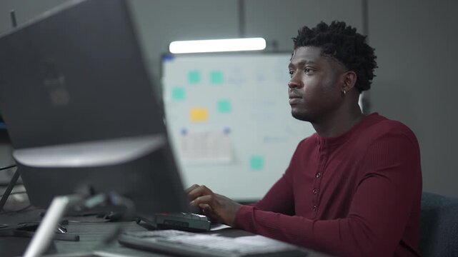 African male software engineer writing program code on multiple desktop screens in a modern office.