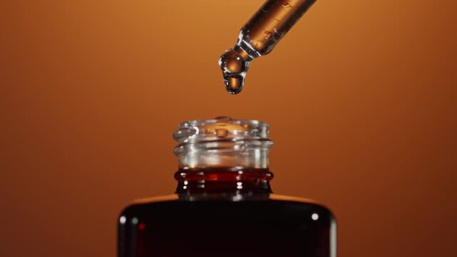 Close-up of essence dripping from glass dropper above amber bottle
