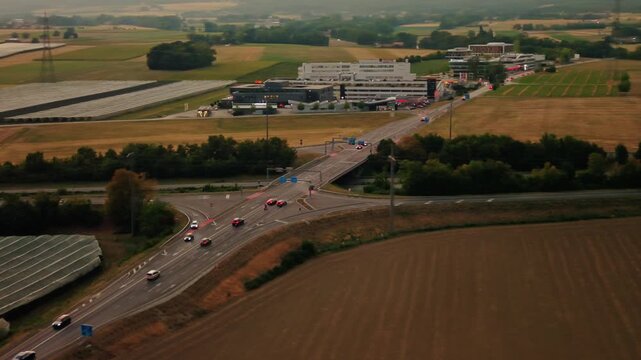 Aerial view of the road intersection at Rte Blanche 1 surrounded by agricultural fields and commercial buildings in Signy-Avenex, Vaud, Switzerland.