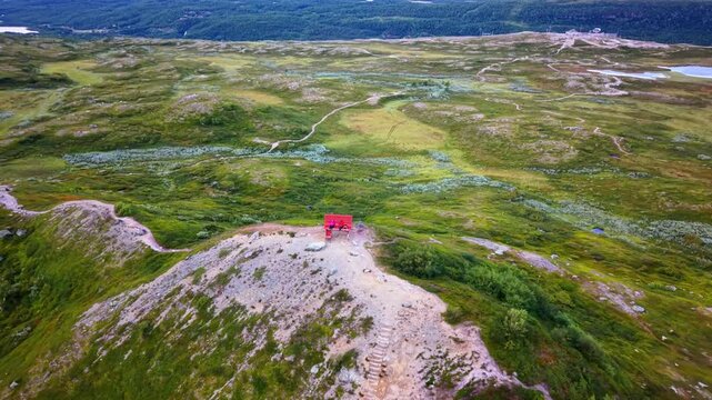 Aerial view of Big Bench 193 on a grassy hill with hikers sitting on the red bench surrounded by winding trails in Tanndalen, Jamtland County, Sweden.