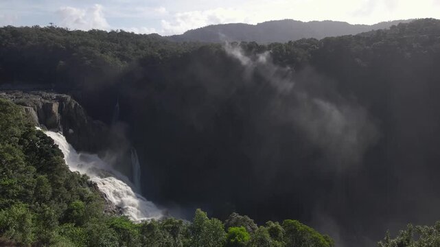 Aerial view of the powerful Barron Falls cascading through the lush tropical rainforest of Kuranda, with mist rising from the gorge under a bright sky in Kuranda, Queensland, Australia.