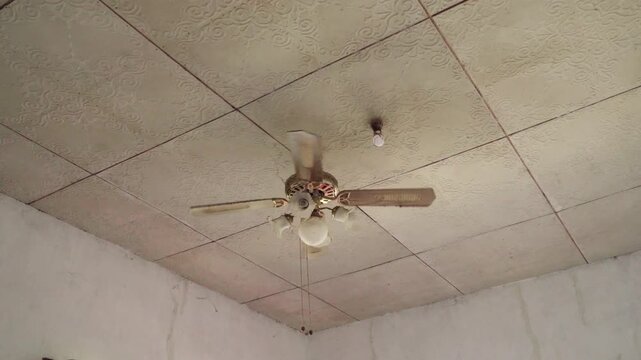 Old ceiling fan spins above textured tile ceiling