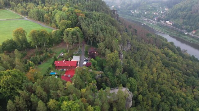 Aerial view of Belvedere Viewpoint surrounded by dense forest, rocky cliffs, and a red-roofed building overlooking the Elbe River in Decin, Usti nad Labem Region, Czechia.