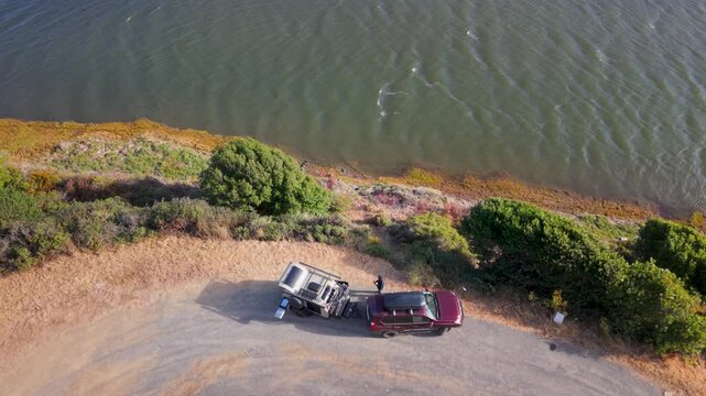 Aerial views show a teardrop camper trailer boon docking on the roadside in California by a lake during summer sunset.