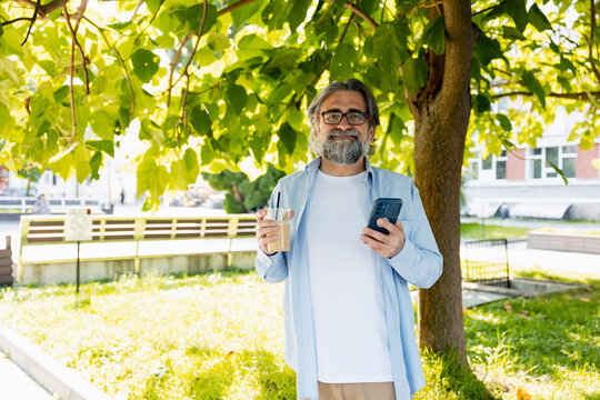 Senior man relaxing in park with smartphone and iced coffee