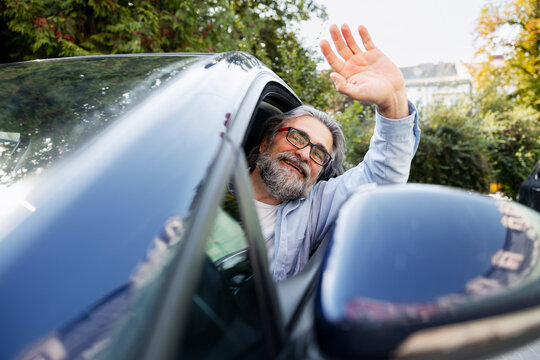 Senior man smiling and waving hand from car