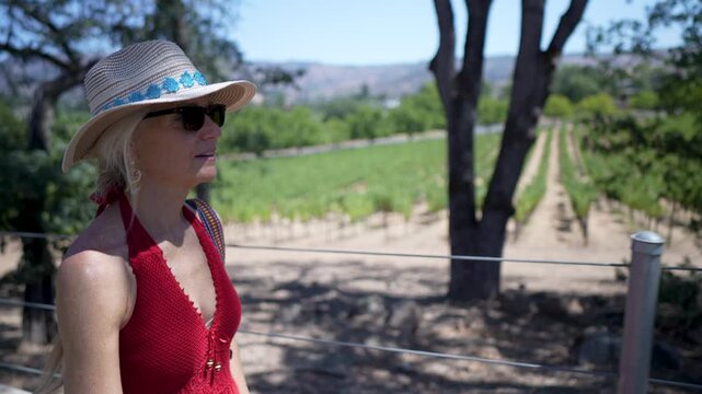 A woman walks through the vineyard, smiles and takes in the sights of the winery on a sunny day in Napa or Sonoma, California