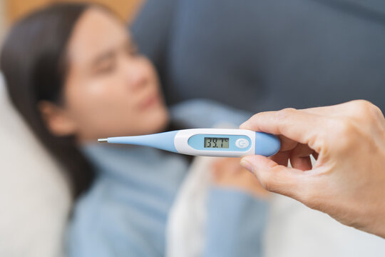 Sick, influenza asian young woman tired have a fever sleep on couch hand holding thermometer for check measure body temperature, illness while rest at home. Health care with disease, pandemic virus.