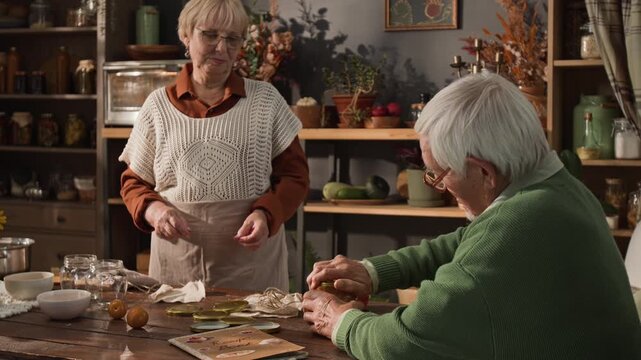 Caucasian senior couple preparing homemade preserves in kitchen, senior man closing jar lid and senior woman wrapping it with cloth. Perfect for retirement lifestyle and organic food marketing