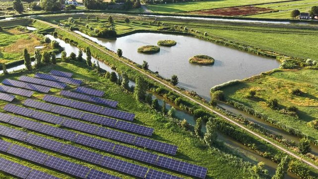 Aerial view of a large solar panel farm situated next to a pond with small islands in the rural landscape of Purmerend, North Holland, Netherlands.