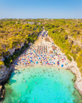 Aerial drone view of a beach with colorful umbrellas and people relaxing. Turquoise crystal clear sea water and white sand during a bright sunny summer vacation.