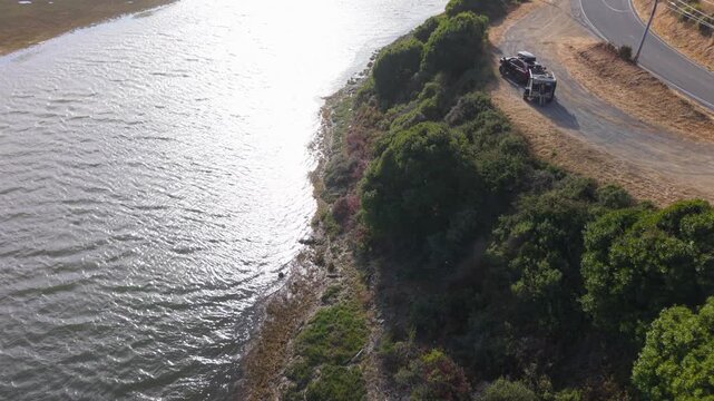 Campers enjoy free camping by the roadside in California. A teardrop trailer sits near the water with a scenic view at sunset.