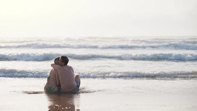 Romantic couple sit in gentle ocean waves, hugging and kissing. Summer beach vacation, love, togetherness, travel, coastal lifestyle, unforgettable moments and romantic getaway concept