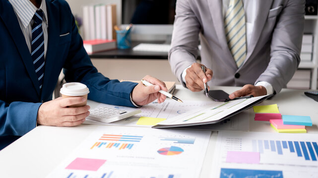 Two men in suits are sitting at a table with papers and pens