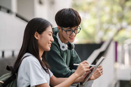 A young man and woman are sitting on a ledge, looking at a tablet
