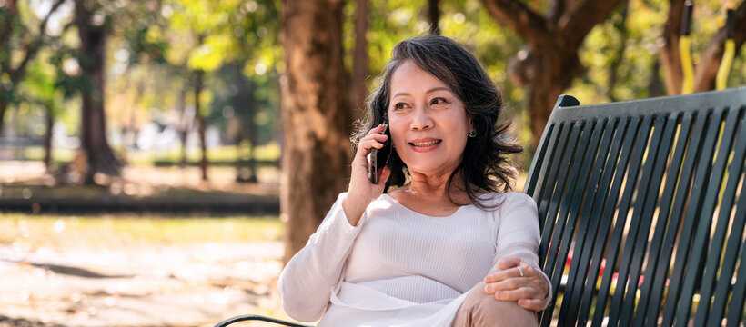 Asian Older Woman Talking on Phone in Park Sitting on Bench Mobile Communication Outdoors Connection Technology Lifestyle Happiness