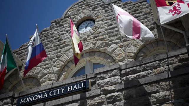 City Hall is shown on a sunny day in Sonoma, California with flags waving. Visitors enjoy the local area and sights.