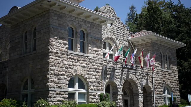 City Hall stands in downtown Sonoma, California, under a bright sun with flags waving. People walk and enjoy the day.