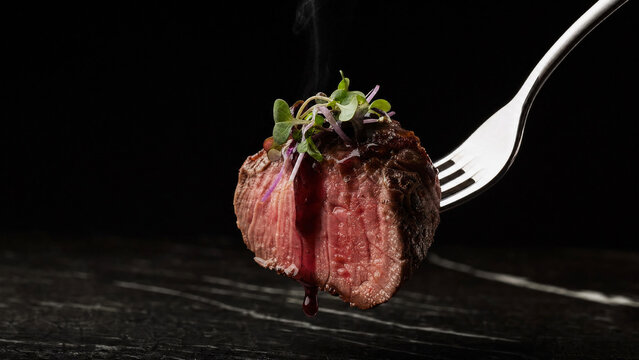 Fork with mediumrare steak bite topped with microgreens