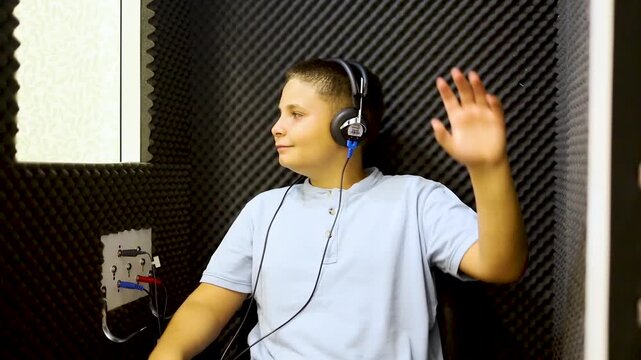 Video of a child undergoing a hearing test in a soundproof booth with headphones. The children raise their hands because they hear a buzzing sound. Concept of hearing problem prevention in children.